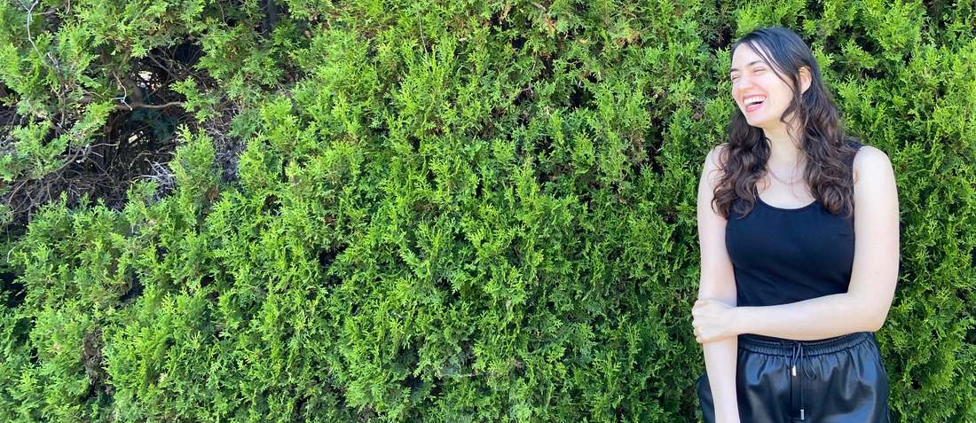 Ida Mayer, smiling, outdoors in front of a hedge